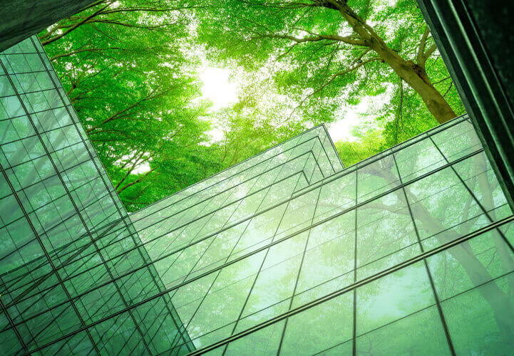 Photo looking up at a building that’s reflecting the green trees all around it.