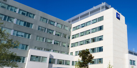 Street level view of a generic hospital building in the middle of the day with bright blue sky.