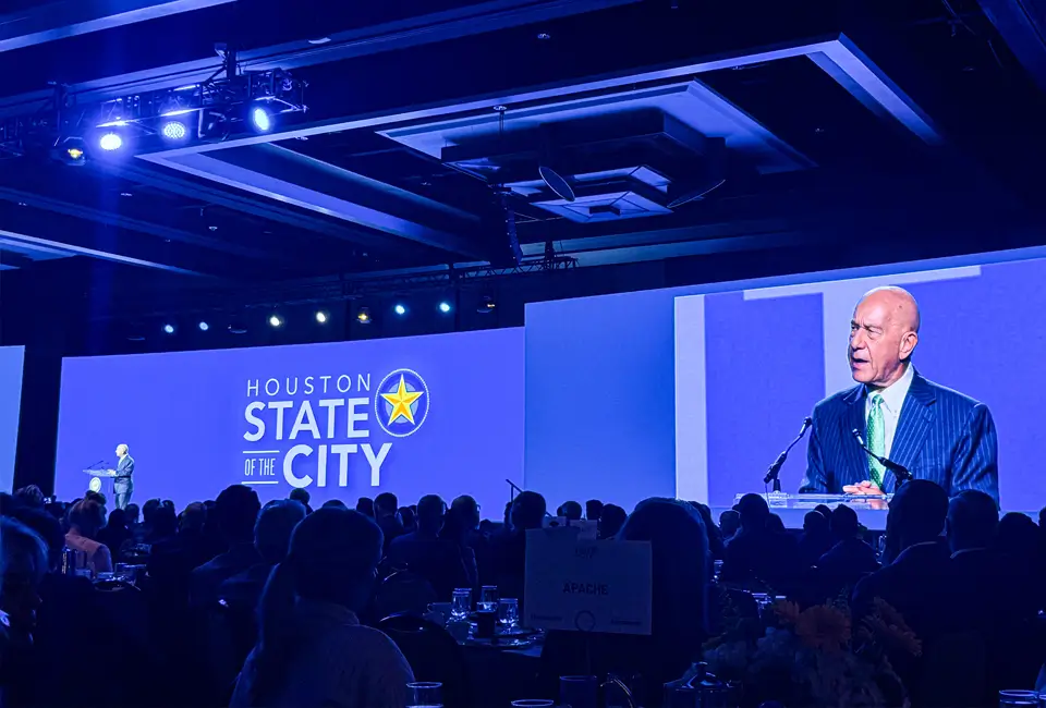 Houston, TX Mayor John Whitmire speaking on stage along with a screen projecting him at the State of the City luncheon.