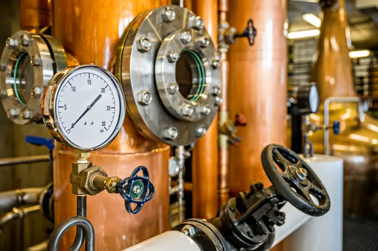 Close up view of a pressure gauge and cooper distilling equipment.